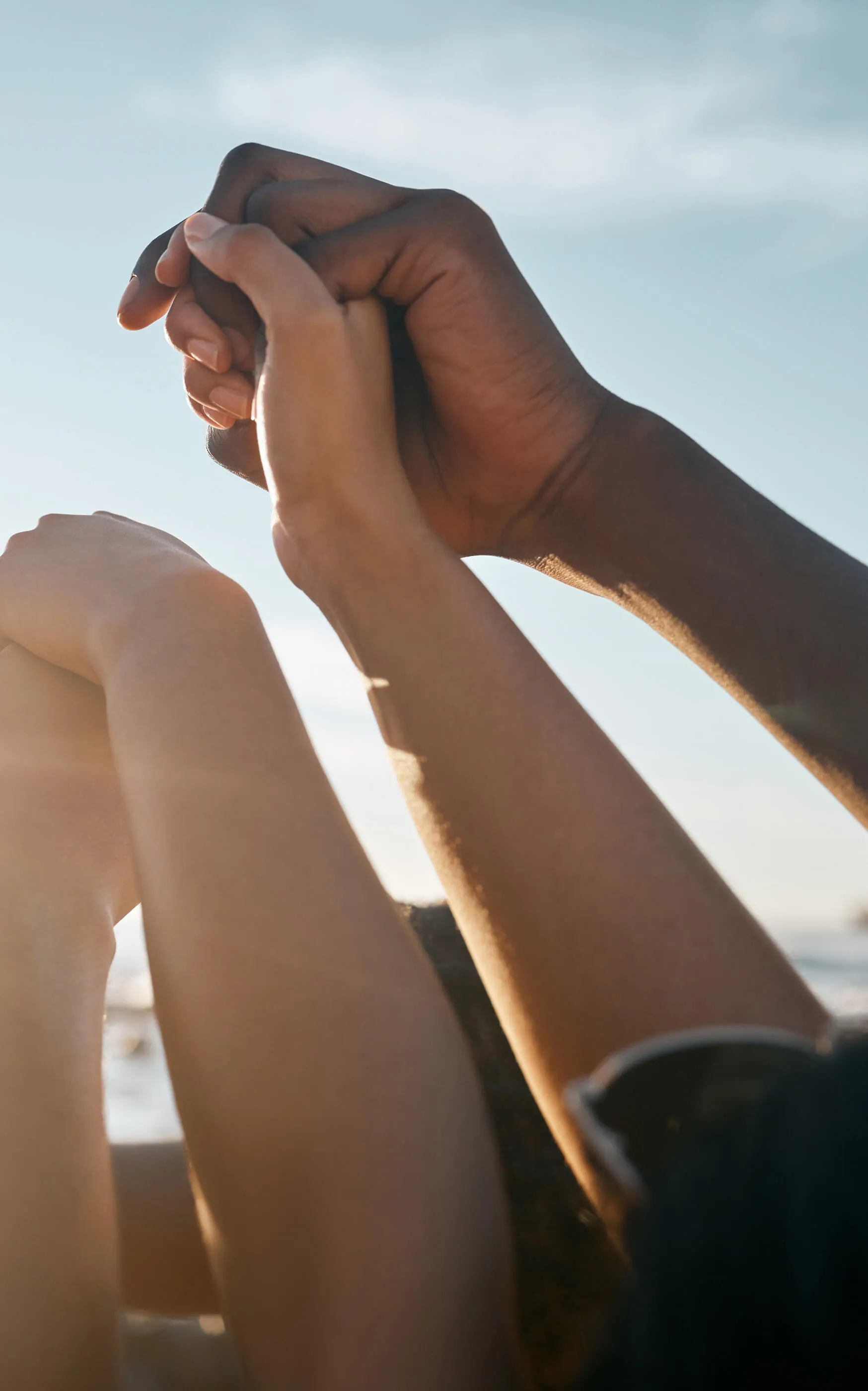 Diverse hands reaching upward and clasping together against a bright blue sky, symbolizing community support